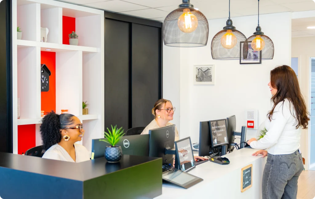 Accueil du cabinet, assistantes et patiente au comptoir