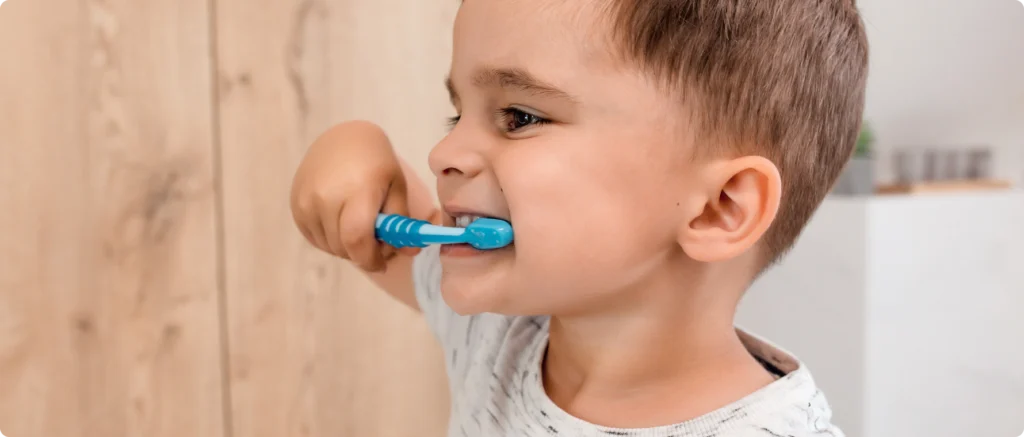 Jeune garçon se brossant les dents avec une brosse bleue