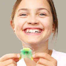 Fillette souriante tenant un appareil dentaire amovible vert